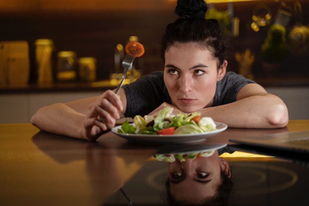 Mulher sentada numa mesa em frente a um prato cheio de salada